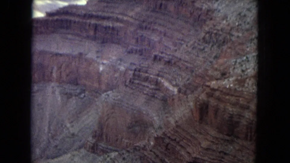 1967 Arizona 8mm frame capturing a broader canyon wall with horizontal strata, reddish rock, dry brush, and soft home-movie exposure.