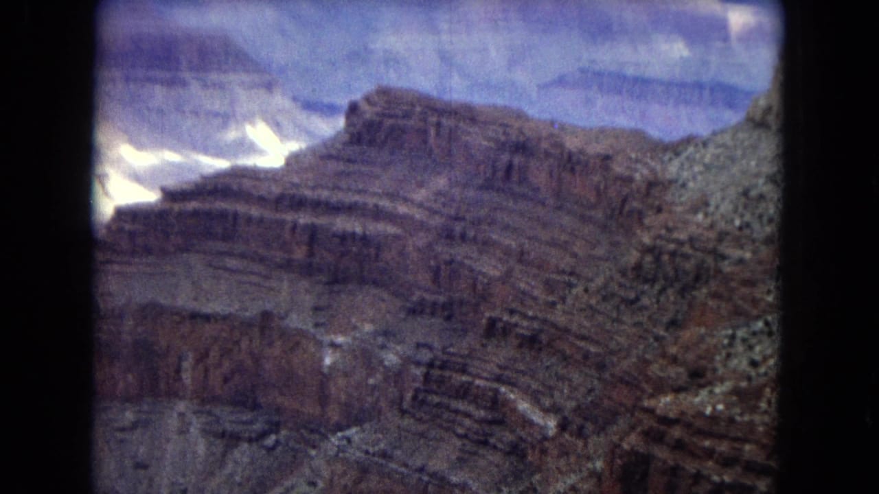 1967 Arizona Grand Canyon aerial view showing stratified canyon walls, shadowed ravines, and pale sunlit rock areas beneath a clouded sky.