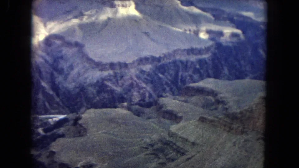 1967 Arizona Grand Canyon aerial view looking down over ridged canyon terrain, pale rock shelves, and winding dark ravines through soft 8mm grain.