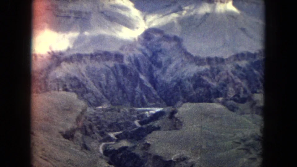 1967 Arizona Grand Canyon aerial frame showing ridged canyon walls, pale terraces, dark drainage lines, and a bright sunlit area along the left edge.