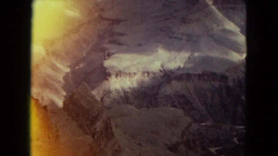 A faded 8mm frame shows rugged canyon terrain and pale snow or rock highlights, partly washed by a yellow-orange light leak at the left edge.