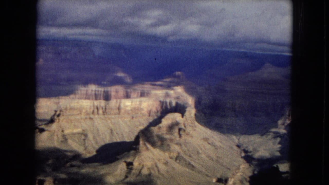 Wide canyon view with sunlit rock shelves and dark ravines beneath clouds.