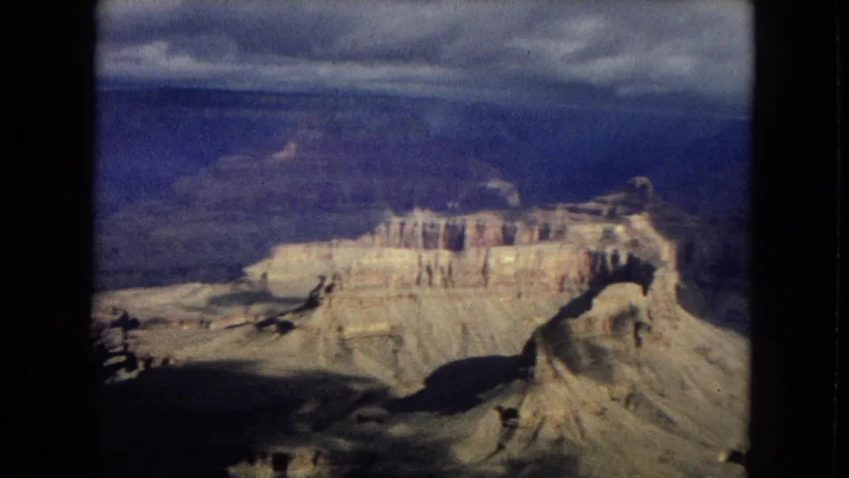 1967 Arizona 8mm frame showing a prominent Grand Canyon butte, horizontal rock layers, blue distant cliffs, and soft home-movie color shift.