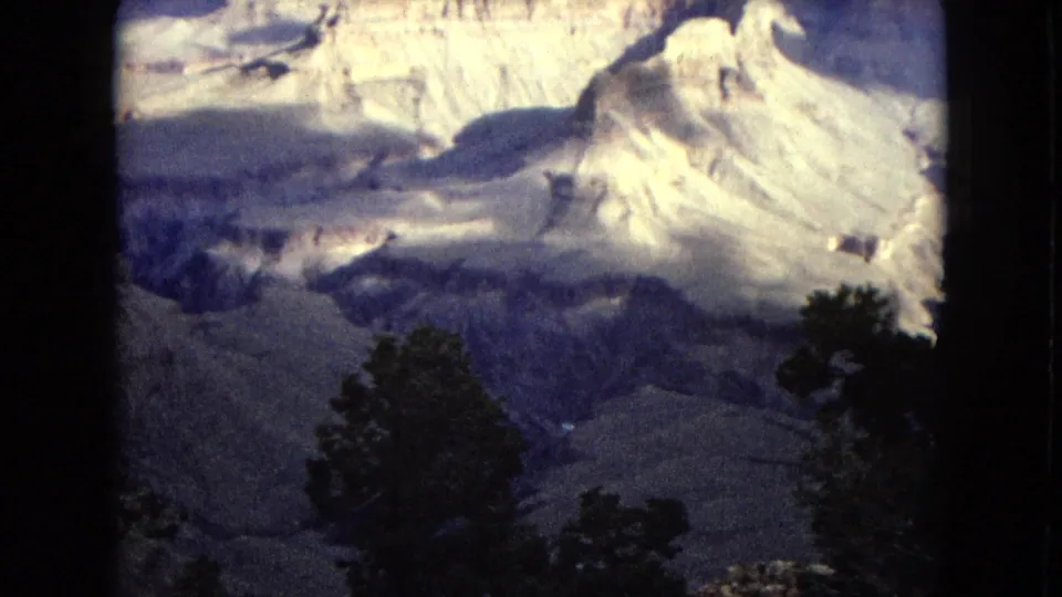 Grand Canyon landscape in 1967 8mm footage, with bright eroded rock faces, shadowed valley floor, dark trees, and layered canyon walls.
