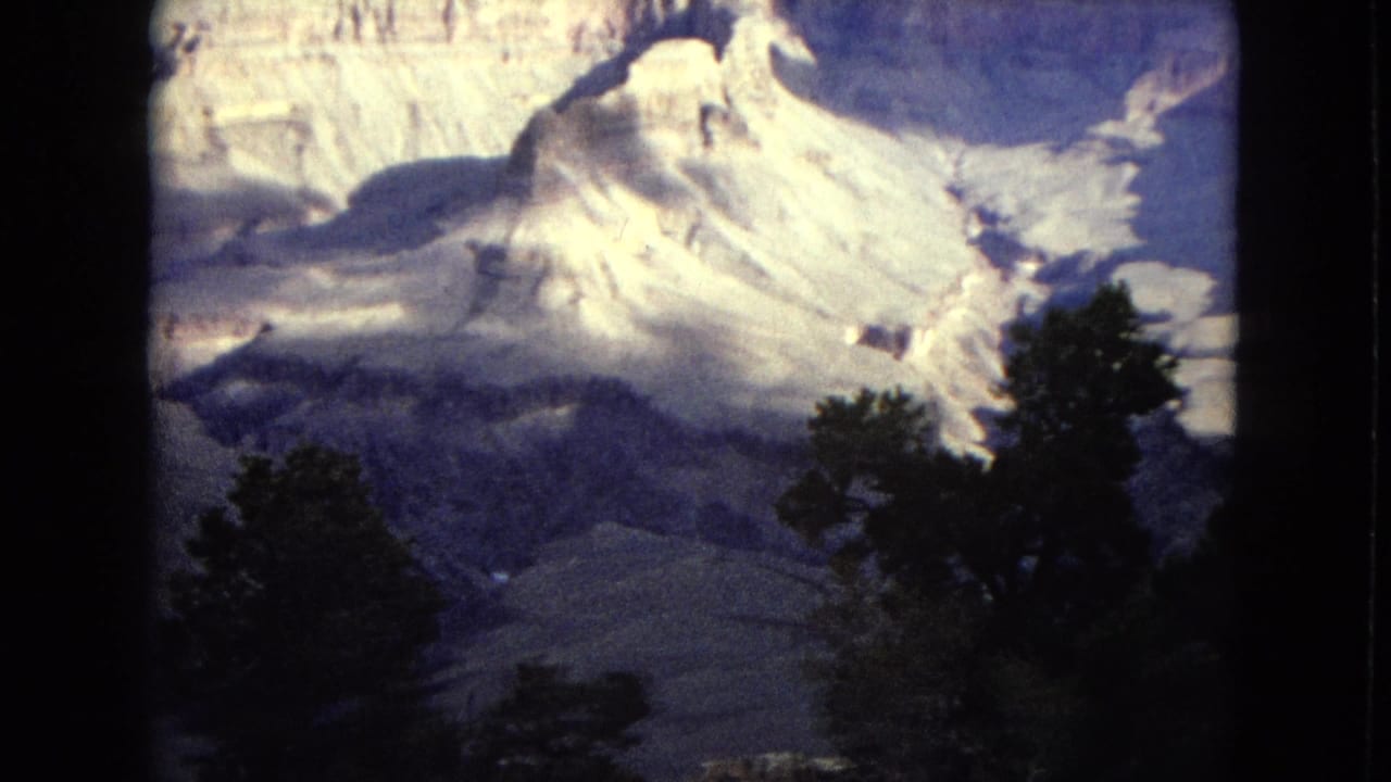 1967 8mm travel footage shows pale Grand Canyon rock formations and a shadowed valley seen past dark pine tree silhouettes.