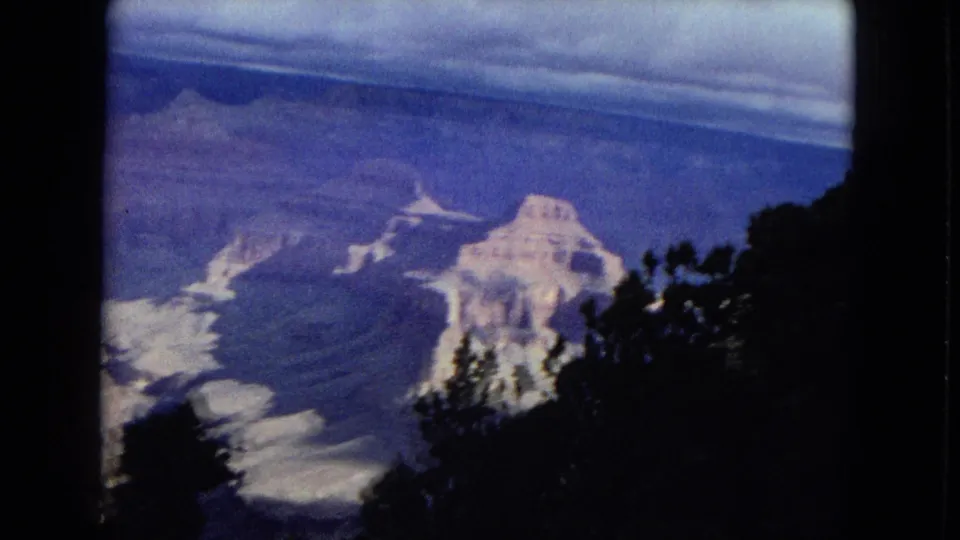 The home-movie camera pans across a Grand Canyon valley, with distant rock formations partly screened by dark trees in the foreground.