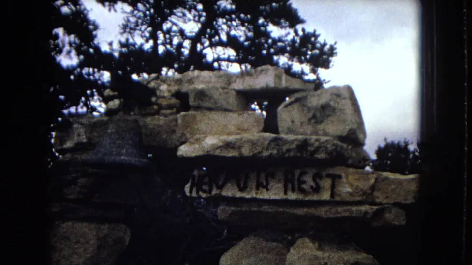 A stone cairn or marker appears beneath a tree, with partially readable lettering including “HEAVEN REST” on one stone.
