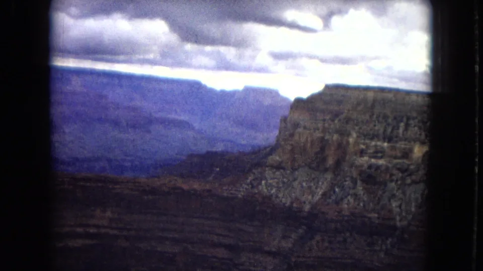 Grand Canyon panorama on 8mm film, showing layered rock formations, a deep valley, and a bright break in the overcast sky.