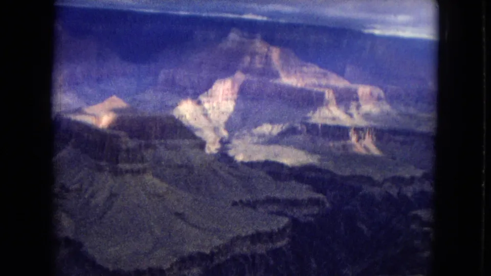 1967 8mm home-movie frame with a sunlit canyon butte, shadowed ravines, and layered rock terraces seen from an aircraft-like viewpoint in Arizona.