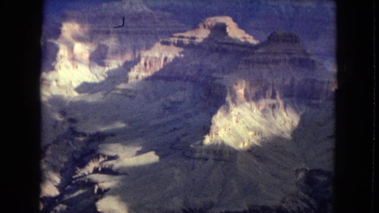 1967 Arizona 8mm frame with a wide Grand Canyon-like panorama, pale cliff faces, darker canyon floors, and evening cloud cover.