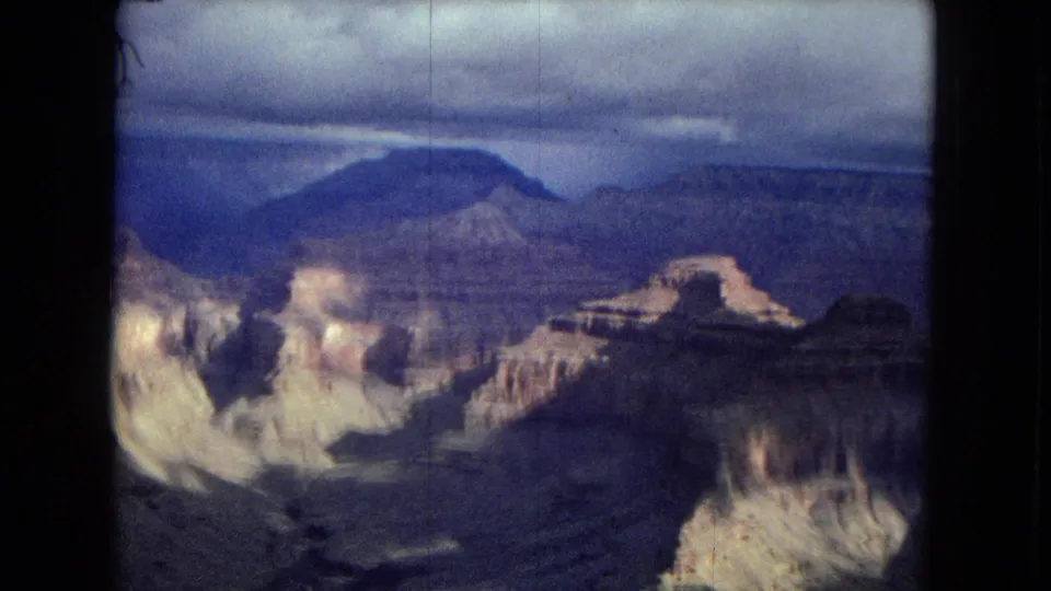 1967 Arizona home-movie still showing a broad canyon overlook with layered formations, subdued evening color, and visible 8mm grain.