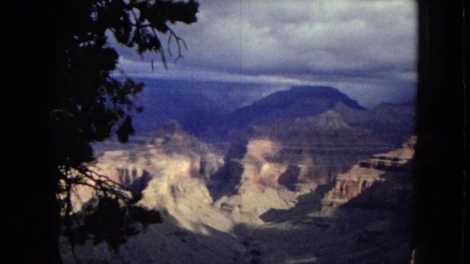 1967 Arizona 8mm frame appearing to show the Grand Canyon from a visitor overlook, with a dark tree branch framing the canyon and cloudy sky.