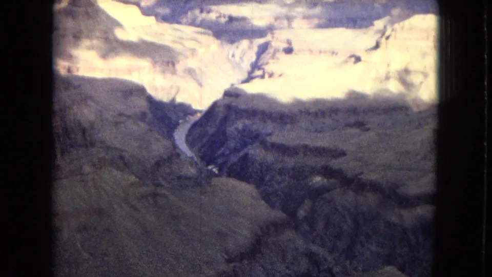 Vintage 8mm frame of the Grand Canyon, showing a bright cloudlit canyon opening, steep rock formations, and the Colorado River curving through the depths.