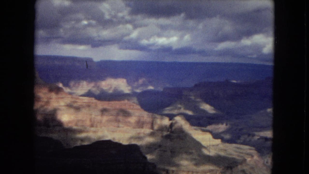 1967 Arizona 8mm frame looking across the Grand Canyon toward sunlit ledges, dark ravines, distant mesas, and a dense cloud bank overhead.