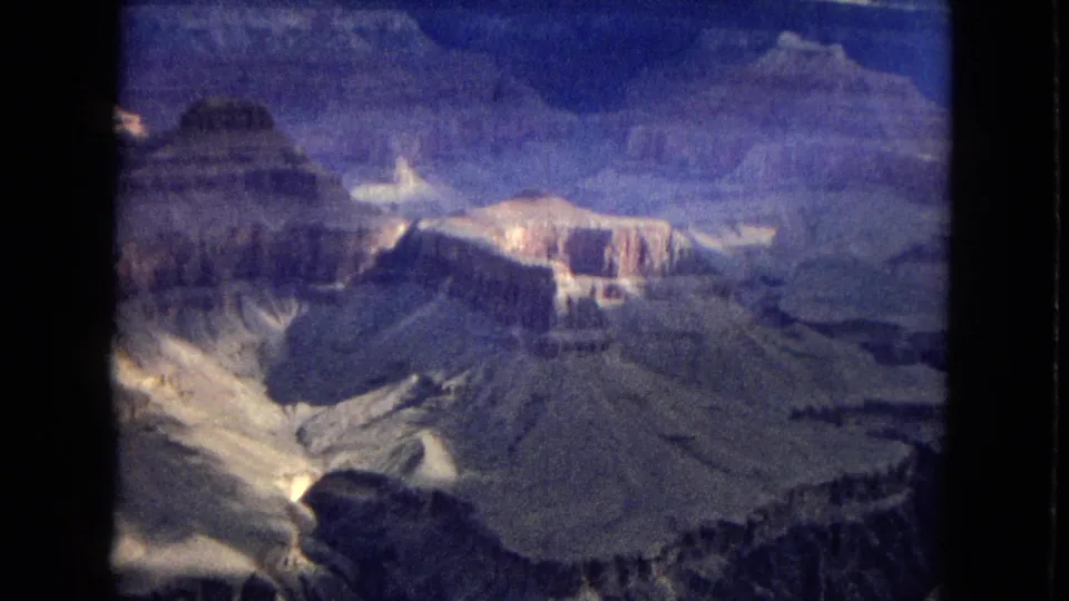 1967 8mm frame of the Grand Canyon with darkened canyon depths, layered cliffs, and shifting light across pale rock formations.