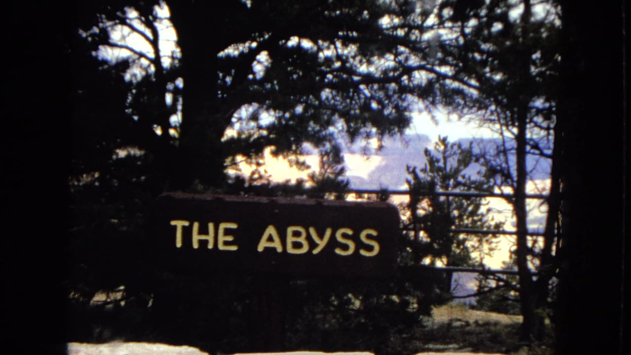 1967 Arizona 8mm frame showing a dark overlook scene with a readable "THE ABYSS" sign, tree silhouettes, and the Grand Canyon visible in the distance.