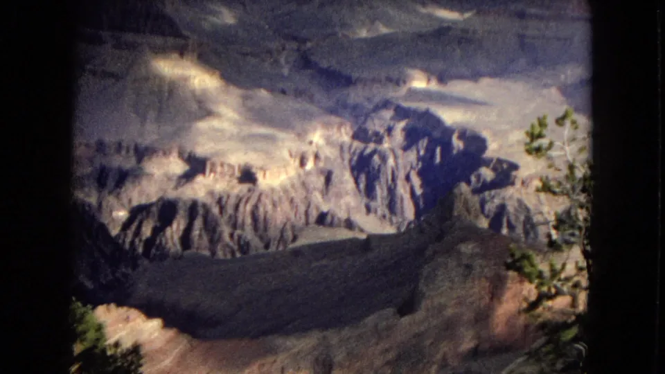 1967 8mm view across Grand Canyon rock formations, with rim vegetation and high-contrast sunlight on layered cliffs.