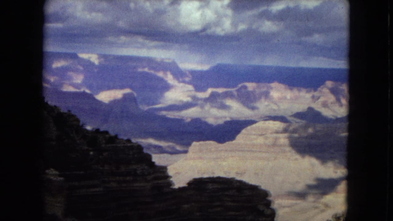 Canyon overlook view with a dark foreground cliff and sunlit formations beyond.