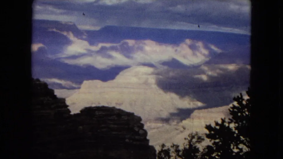 1967 8mm Arizona home-movie footage showing bright Grand Canyon rock formations beyond a dark foreground ridge, with soft focus and blue-gray sky tones.