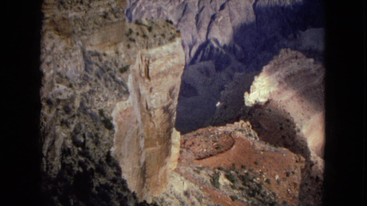 Steep canyon rock face with shadowed ravine and reddish slope below.