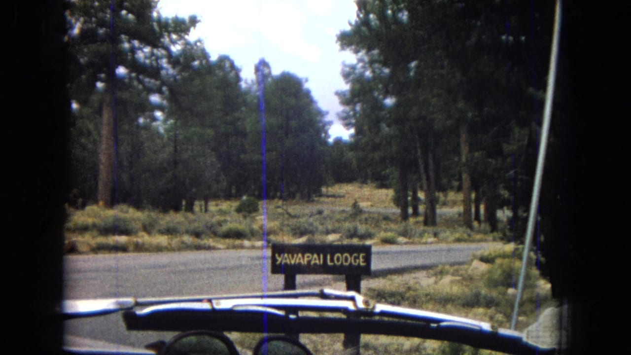 1967 Arizona 8mm frame showing a wooden Yavapai Lodge roadside sign among pine trees, filmed from a car at the lodge entrance.