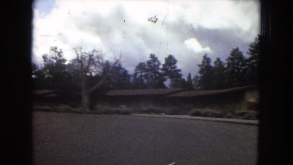 1967 Arizona 8mm frame with a low lodge building under a cloudy sky, framed by trees and dark scan edges from the home-movie film.