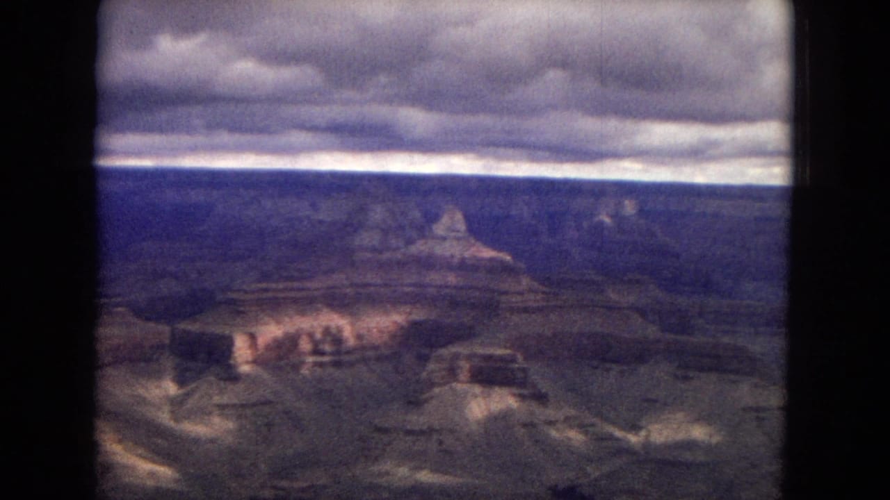 1967 8mm home-movie frame showing a broad canyon view in Arizona with layered rock formations and a heavy cloud bank overhead.