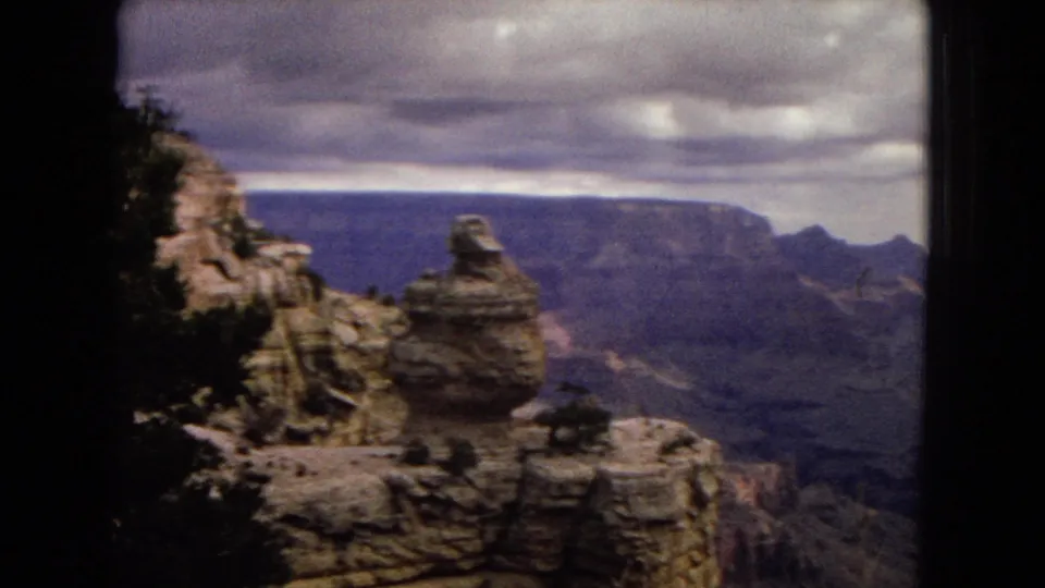 Grand Canyon overlook view with a prominent rock formation in the foreground and layered canyon walls receding under an overcast sky.
