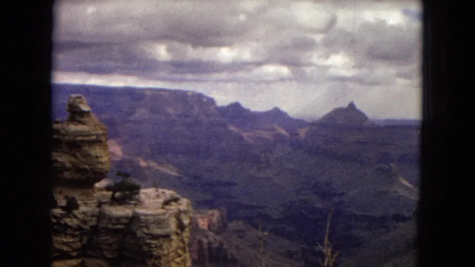 Grand Canyon panorama from a high viewpoint, with foreground rock ledges, distant buttes, and broad canyon terrain visible through faded 8mm color.