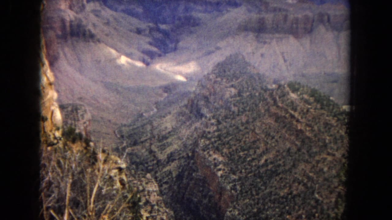 Wide canyon basin with layered rock slopes, wooded ridges, and pale snow patches.