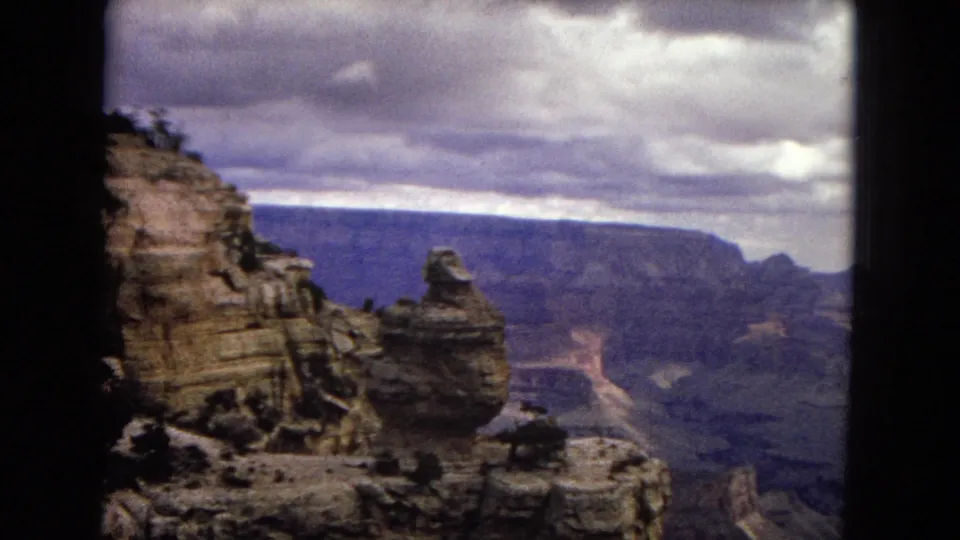 1967 Arizona 8mm frame showing a canyon overlook, a rounded rock formation, layered distant cliffs, and a cloudy sky with dark film borders.