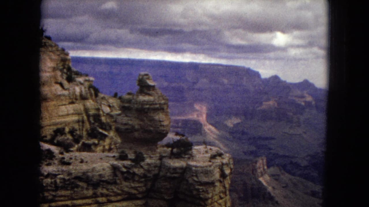 1967 8mm home-movie view of Grand Canyon cliffs in Arizona, with a rock outcrop at left, distant canyon walls, and dark framing around the scene.
