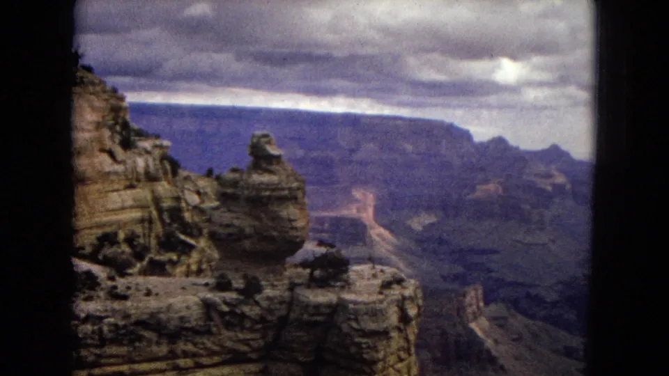 1967 8mm home-movie view of Grand Canyon cliffs in Arizona, with a rock outcrop at left, distant canyon walls, and dark framing around the scene.