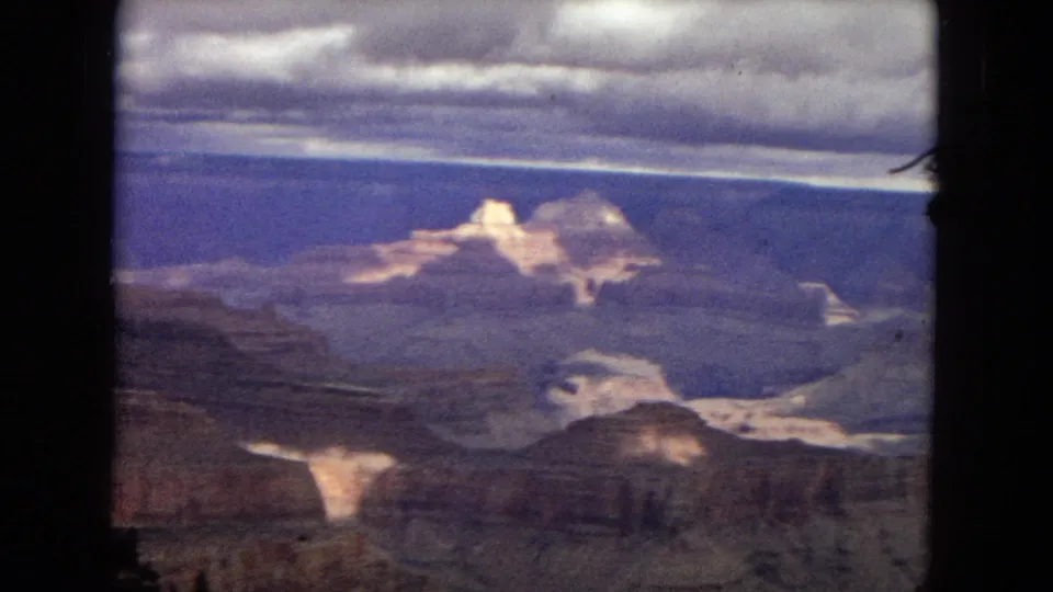 1967 8mm Grand Canyon panorama showing pale sunlit rock formations, layered canyon depths, and a broad cloudy sky from a visitor overlook.