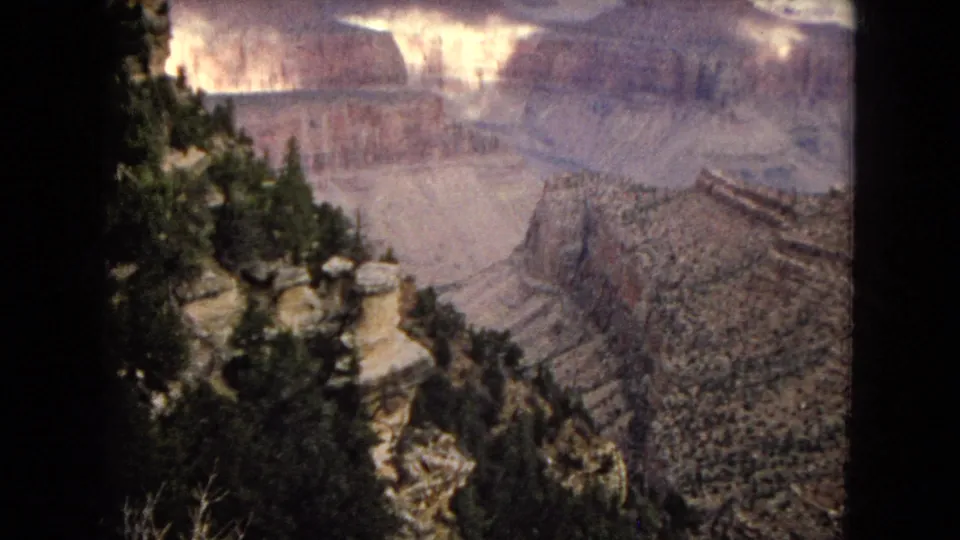1967 Arizona 8mm frame looking from a pine-edged cliff across layered canyon walls and distant rock formations.