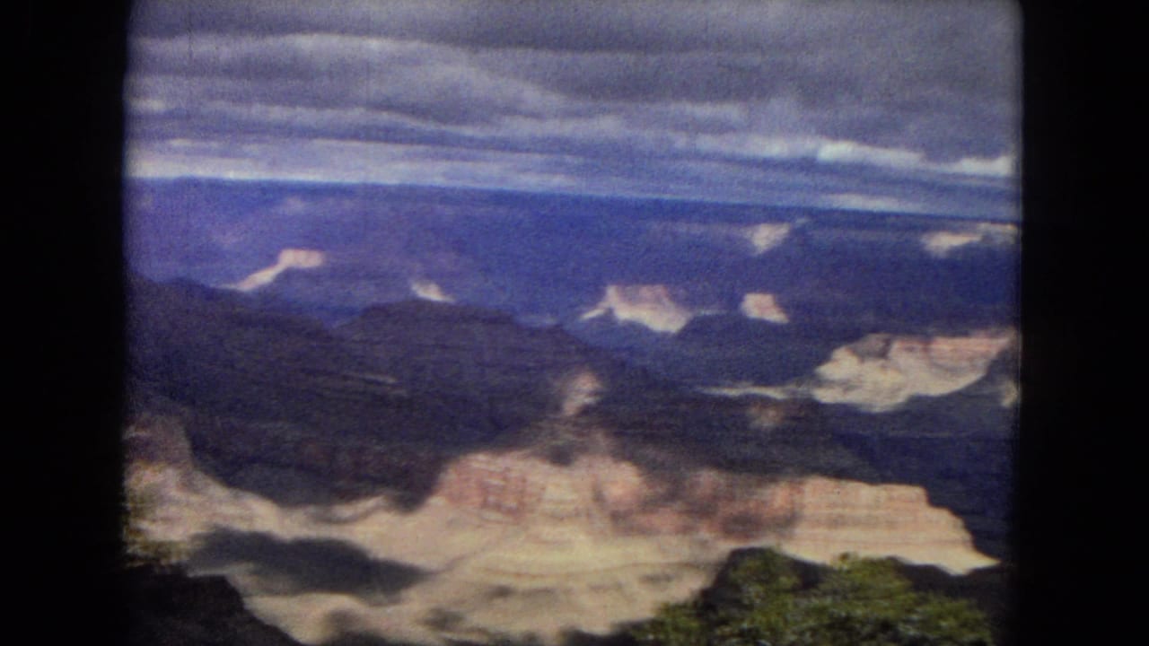 Wide canyon view with pale rock ledges, dark ravines, and low clouds overhead.