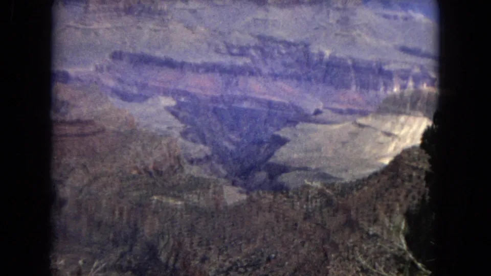 1967 8mm frame of the Grand Canyon with broad exposed rock layers, deep cuts through the landscape, and a dark central film border from the scan.
