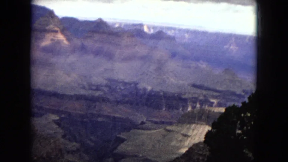 1967 8mm home-movie frame showing a broad Grand Canyon panorama beneath a bright cloudy sky, with shadowed cliffs and dark film borders at the sides.