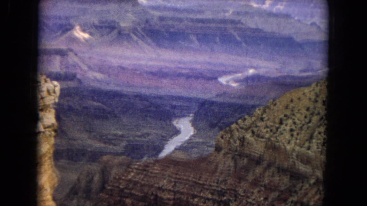 1967 8mm home-movie frame of the Colorado River visible far below layered Grand Canyon cliffs in Arizona, with faded color and soft handheld framing.