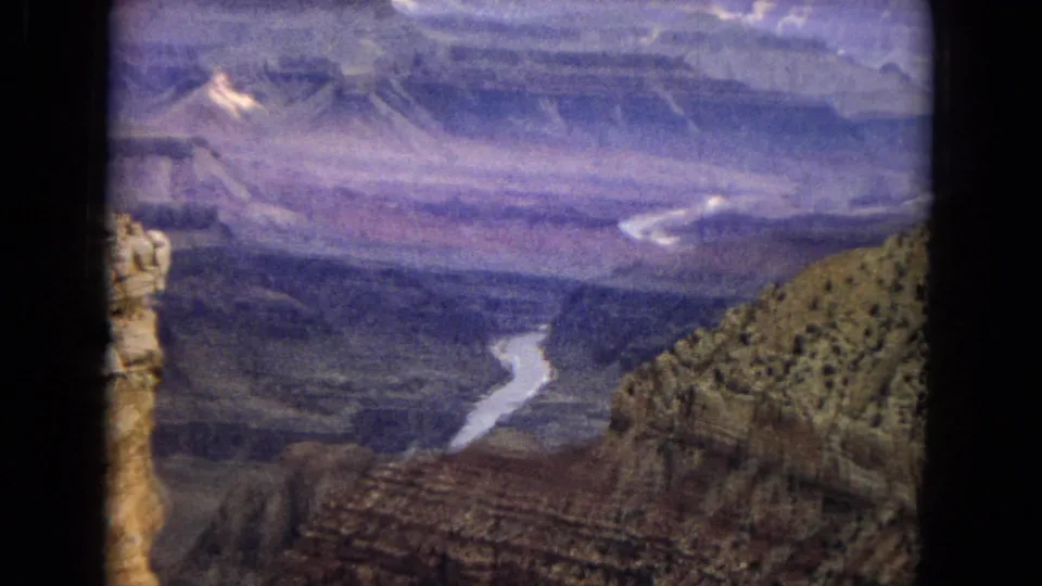 1967 8mm home-movie frame of the Colorado River visible far below layered Grand Canyon cliffs in Arizona, with faded color and soft handheld framing.