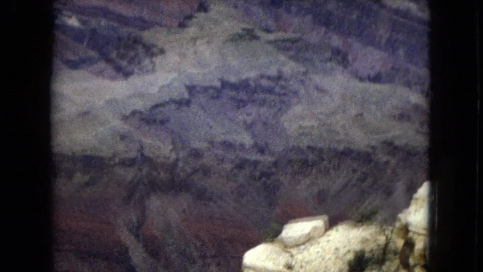 1967 8mm home-movie frame of the Grand Canyon in Arizona, showing shadowed layered rock walls and a pale ledge near the lower right edge.