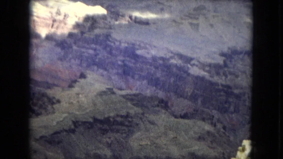 1967 8mm home-movie frame of the Grand Canyon in Arizona, with stratified slopes, a bright sunlit rock area near the rim, and deep shadowed formations below.