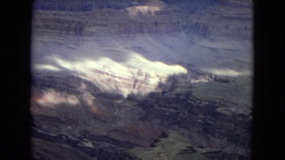 1967 8mm home-movie frame of the Grand Canyon in Arizona, showing a pale illuminated rock formation across the middle distance with darker eroded strata beneath it.