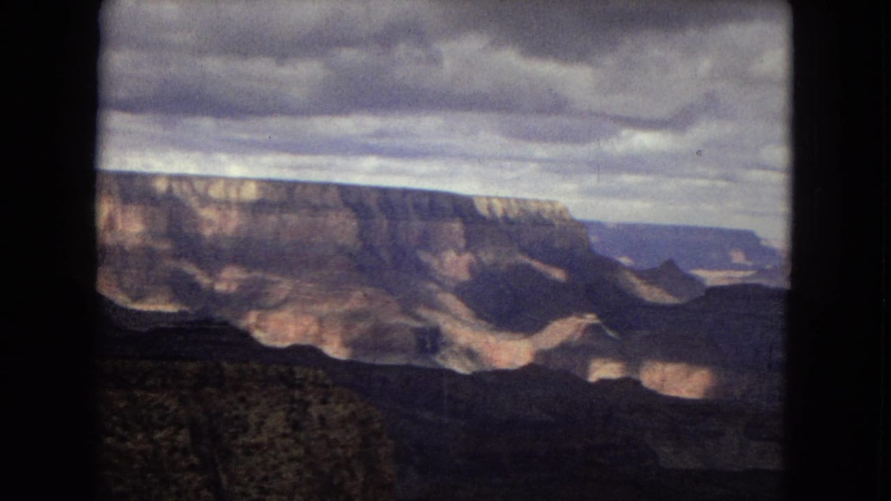 1967 8mm Grand Canyon panorama showing broad rock formations, distant blue-toned mesas, and shifting cloud shadow across the valley.