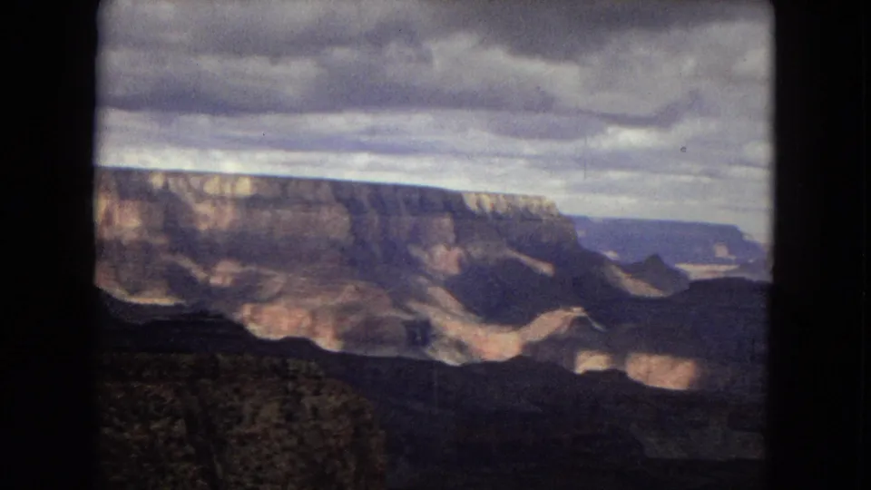 1967 8mm Grand Canyon panorama showing broad rock formations, distant blue-toned mesas, and shifting cloud shadow across the valley.