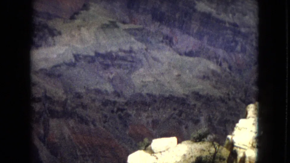 1967 Arizona 8mm frame showing layered canyon formations from a high overlook, with pale foreground rock and dark film edges visible.