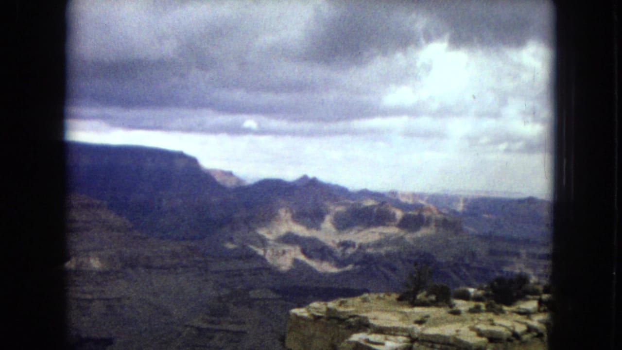 Wide canyon vista under a cloudy sky with rocky overlook in the foreground.
