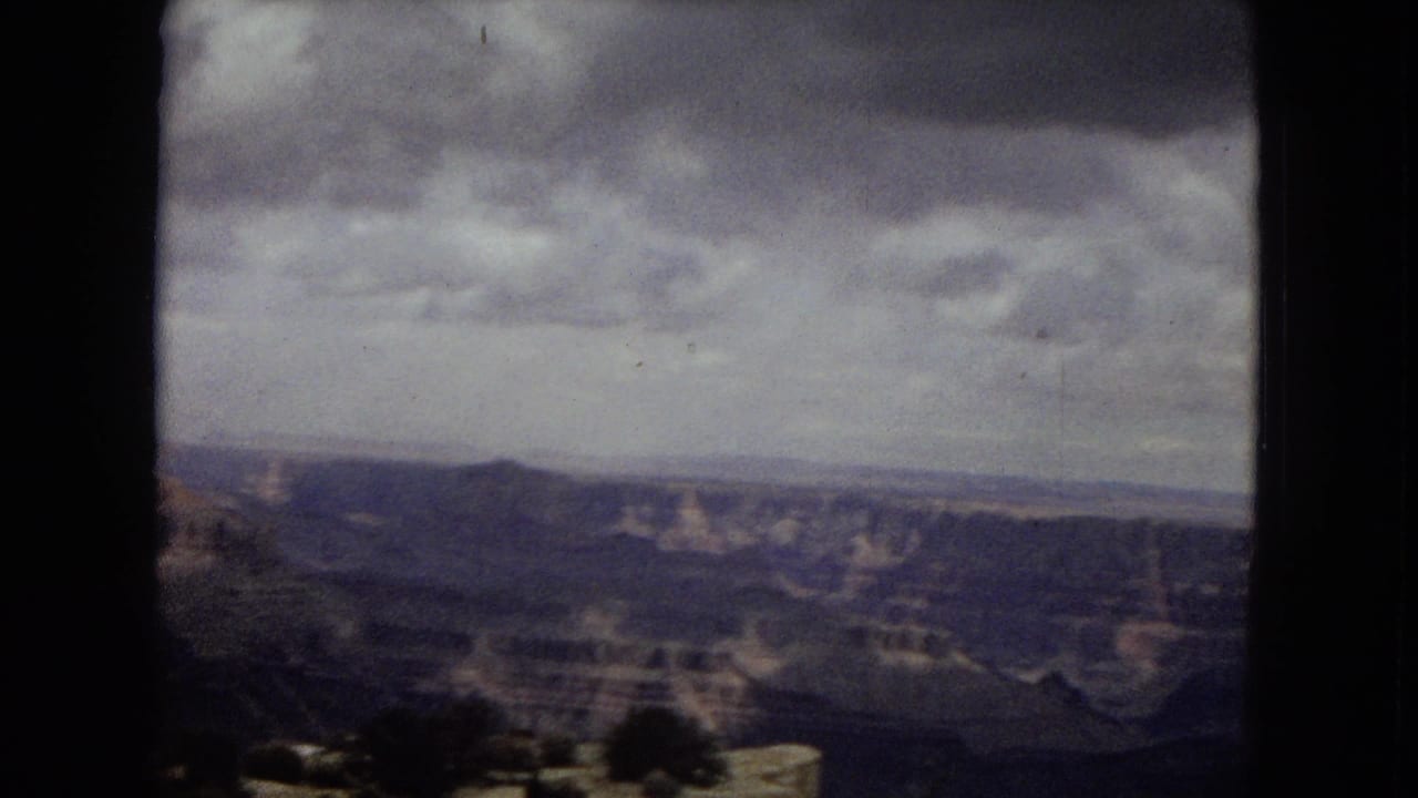 1967 Arizona 8mm frame showing a broad Grand Canyon overlook under overcast skies, with distant layered canyon walls and soft home-movie grain.