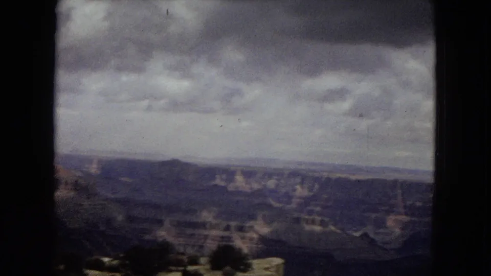 1967 Arizona 8mm frame showing a broad Grand Canyon overlook under overcast skies, with distant layered canyon walls and soft home-movie grain.