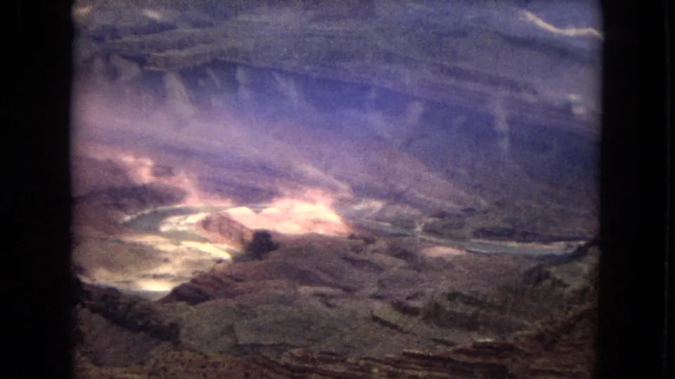 1967 Arizona 8mm frame showing a canyon basin with a bright smoky or dusty disturbance near pale winding ground features and surrounding rock walls.